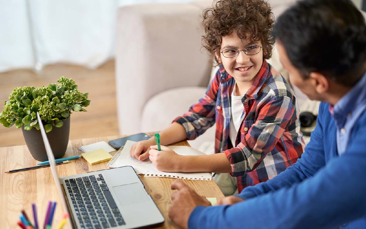 Portrait of joyful young boy enjoying Spanish class together with his father, using laptop while sitting at the desk at home.