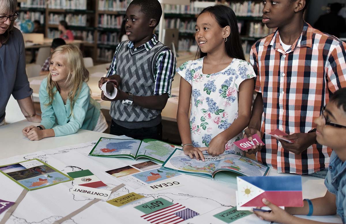 A small group of diverse students standing around a table listening to their teacher during a geography lesson.