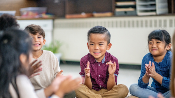 Small group of children sitting in a circle clapping hands and smiling